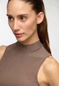 Top senza maniche marrone a collo alto realizzato in materiale a coste con una texture liscia, caratterizzato da un design aderente e un leggero splendore.