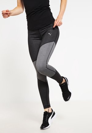 Leggingit mustat ja harmaat kuviot, joissa on tiukka muotoilu, verkko-yksityiskohtia ja logo sivussa. Yhdistetty mustiin urheilujalkineisiin.