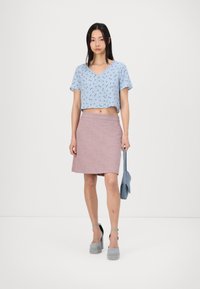 Top corto de estampado floral azul con mangas cortas, combinado con una falda A-line de color rosa claro. La modelo lleva zapatos de platform grises y sostiene un bolso azul.