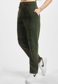 Grønne joggebukser med et teksturert svart geometrisk mønster, elastisk midjebånd med snor, og sidelommer, kombinert med hvite joggesko.