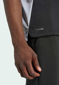Černé sportovní tričko s šedými akcenty, vyrobené z prodyšného materiálu. Obsahuje štítek "CLIMACOOL" a přiléhavý střih s texturovaným povrchem.