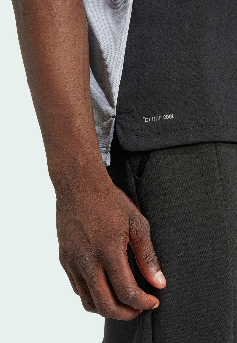 Schwarzes Sportshirt mit grauen Akzenten, aus atmungsaktivem Material gefertigt. Enthält das Label "CLIMACOOL" und eine taillierte Passform, die eine strukturierte Oberfläche zeigt.