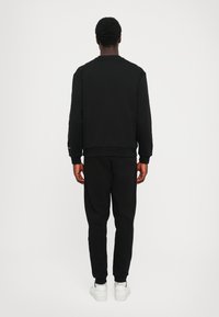 Black sweatshirt and joggers ensemble, made of soft fabric with a ribbed texture. Features a crew neck and tapered pants, paired with white sneakers.