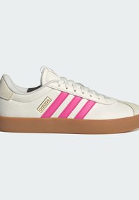 Baskets basses blanches Adidas avec des bandes roses, une semelle en gomme, un lacet sur le devant et le logo Adidas près du talon sur un fond clair.