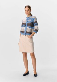 Gehaakte cardigan in blauw, bruin en crème met een ronde halslijn en knoopsluiting. Beigekleurige A-lijn rok met zakken en platte schoenen.