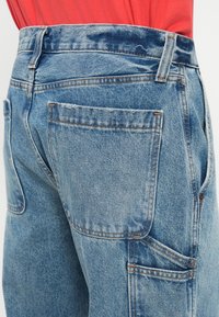 Svijetloplave traper cargo hlače s višestrukim džepovima, vidljivim šavovima i izblijedjelom teksturom. Pojas ima petlje za remen.