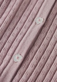 Ljust rosa stickad tyg med vertikalt ribbmönster, med två klara blomformade knappar som accenter.