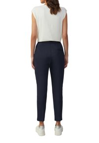 Pantalons ajustés bleu marine en tissu texturé, dotés d'une poche arrière et d'une ceinture confortable. Associés à un haut blanc et des sneakers.