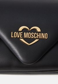 Černá kožená psaníčko se zlatým logem "LOVE MOSCHINO" a detailem srdce. Disponuje hladkým povrchem a uzavřením ve stylu obálky.