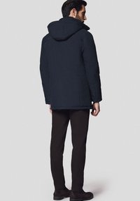 Ciemnoniebieska pikowana kurtka z kapturem, posiadająca cztery kieszenie, zestawiona z ciemnobrązowymi spodniami i botkami za kostkę.