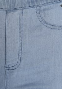Light blue denim fabric showing a close-up of a pocket with visible stitching detail and a slightly textured surface.