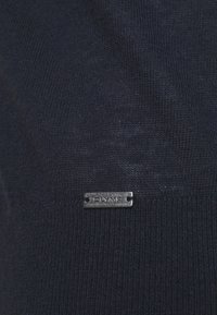 Navy knitted fabric with a smooth texture and metallic logo tag labeled "OLYMP" in silver. The fabric is soft and closely woven.
