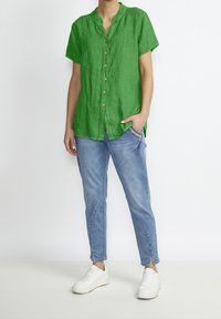 Green linen short-sleeve shirt with a buttoned front and small collar, paired with light blue tapered jeans and white sneakers.
