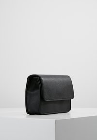 Czarna skórzana torebka na ramię z klapką. Gładka tekstura i prostokątny kształt. Kompaktowy design z subtelnymi detalami przeszyć.