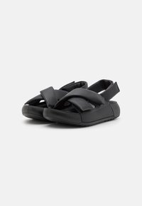 Sorte sandaler med en myk, overlappende stroppedesign. Laget av et syntetisk materiale, med en polstret såle og justerbar bakre stropp.