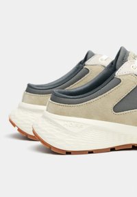 Zapatillas deportivas grises y beige con material de ante y malla, con una suela blanca texturizada y detalles de goma.