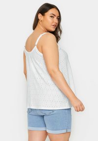 Camiseta sin mangas blanca con pequeños patrones de puntos negros, tirantes ajustables y un corte holgado, combinada con pantalones cortos de mezclilla.