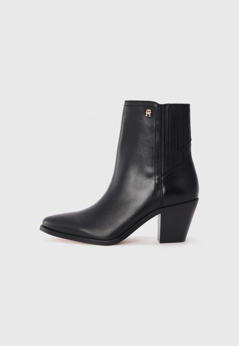 Svart lær ankelstøvlett med spiss tå, elastiske sidestykker og firkantet hæl. Har et lite gulllogo som aksent.