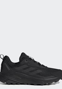 Zwarte Adidas Terrex trailrunning schoen met een gestructureerde zool en mesh bovenwerk, gezien vanaf de zijkant op een witte achtergrond.