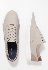 Beiga kanvas sneakers med vita gummisulor, rund tå och bruna läderaccenter. Snördesign med silverfärgade öglor och randig foder.