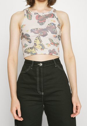 Woman wearing a sleeveless crop top with colorful butterfly prints and high-waisted black pants with white stitching.