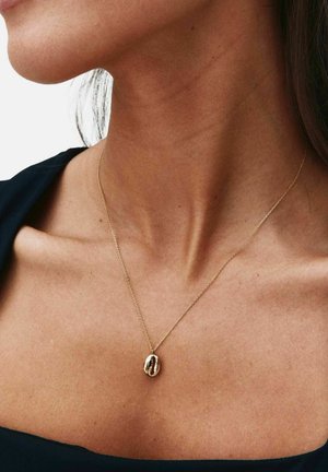 Približna snimka ženskog vrata sa nježnim zlatnim lancem i privjeskom u obliku zlatnog zrna kave na tankom lancu.