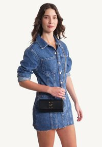 Robe chemise en denim bleu à manches longues et deux poches avant, accompagnée d'un sac bandoulière en cuir noir avec des détails en or.