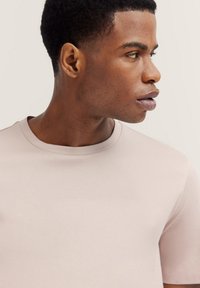 Light pink crew-neck t-shirt with short sleeves, made of smooth fabric. Slim fit with a soft texture, highlighting the neckline detail.