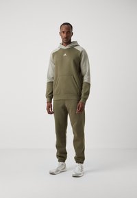 Tuta verde oliva con cappuccio e tasca a marsupio, con maniche grigio chiaro, polsini elasticizzati e pantaloni a sigaretta abbinati.