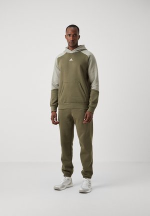 Tuta verde oliva con cappuccio e tasca a marsupio, con maniche grigio chiaro, polsini elasticizzati e pantaloni a sigaretta abbinati.