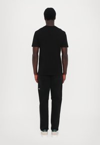 Schwarzes T-Shirt mit kurzen Ärmeln und weiten schwarzen Jeans. Die Schuhe sind cremefarben mit grünen Akzenten. Das Design ist minimalistisch, ohne sichtbare Logos.