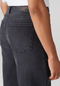 Vaqueros de mezclilla oscura con corte recto. Presentan bolsillos traseros y una cintura alta. El material tiene una textura suave con un desvanecimiento mínimo.