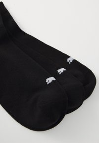 Schwarze Kniestrümpfe aus glattem Stoff, mit einem weißen Bärenlogo, das nahe der Oberseite gestickt ist. Drei Paare gruppiert.