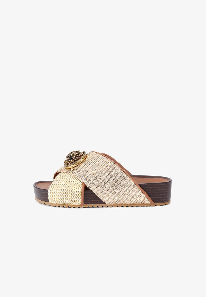 Mocassin tissé beige avec une semelle marron épaisse. Présente un accent floral métallique décoratif sur la sangle entrecroisée. Surface texturée.