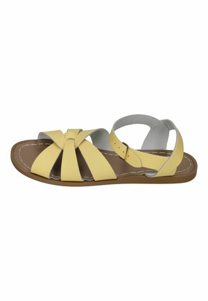 Yellow open-toe flat sandal with buckle ankle strap and multiple straps crossing over the foot on a brown sole with white stitching.