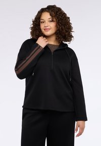 Sudadera negra con capucha y cremallera de cuarto, con franjas marrones en las mangas. Tela suave con un ajuste relajado y mangas largas.