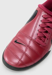 Sapatilha atlética em couro vermelho com design acolchoado, detalhes em preto, sola preta e atacadores em bordeaux. Apresenta um pequeno logotipo preto na lateral.