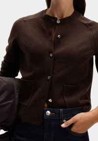 Brązowy sweter z dzianiny z okrągłym dekoltem, z pięcioma guzikami z przodu, dwiema kieszeniami z przodu i ribbowanymi mankietami.
