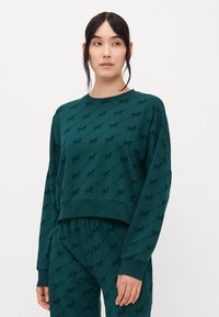 Teal ylityksellinen huppari, jossa on musta logopainatus kauttaaltaan. Valmistettu pehmeästä kankaasta, jossa on pitkät hihat ja pyöreä kaula-aukko.