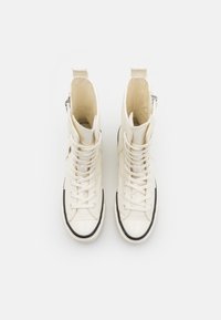 Korkeavartiset sneakerit off-white kankaasta mustilla kumipohjilla. Varustettu edestä kiristettävällä nauhalla ja sivuvetoketjulla helppoa pääsyä varten.