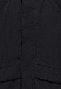 Gros plan d'un tissu noir avec des coutures visibles, probablement une partie d'un vêtement ou d'un article textile.