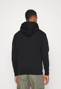 Sudadera con capucha negra de corte relajado, con una gran capucha y puños acanalados. Fabricada con un tejido suave, presenta un diseño simple y sin adornos.