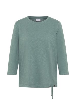 Haut à manches longues de couleur teal en tissu texturé, avec un col rond et un détail de lien latéral ajustable pour un ajustement personnalisable.