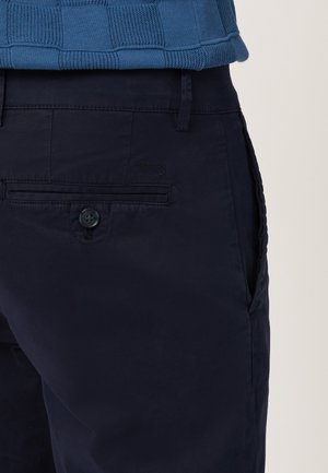 Marineblauwe broek met knoopsluiting, zijzakken en een achterzak, voorzien van een subtiel geborduurd logo. Gladde katoenen stof, slim fit.