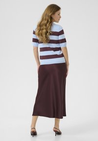 Top a righe blu e bordeaux in maglia con maniche corte abbinato a una gonna maxi in satin bordeaux, caratterizzata da una texture liscia e una silhouette fluttuante.