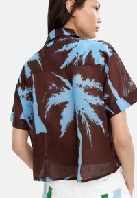 Koszula z krótkim rękawem, w brązowo-niebieski wzór, z nadrukiem palm, wykonana z lekkiego materiału i o luźnym kroju.