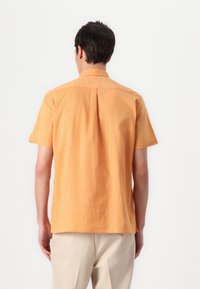 Camisa de manga curta, com colarinho, em tecido texturizado de laranja claro, apresentando um corte descontraído e detalhe de pregas nas costas.