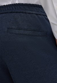 Ciemnoniebieskie spodnie z fakturowanej tkaniny, z tylną kieszenią i elastycznym paskiem w talii. Projekt jest prosty, z czystymi liniami i bez widocznych ozdób.