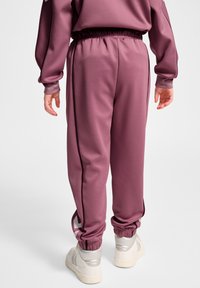 Lyserøde sweatpants med en elastisk talje, smalle manchetter og sidelommer. Materialet er glat med en let skinnende overflade.