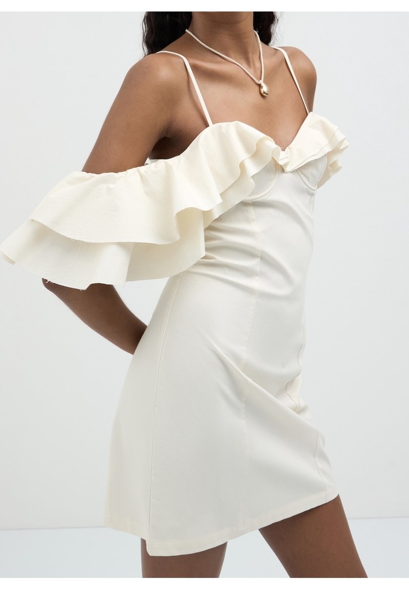 White off-the-shoulder dress with layered ruffle sleeves, fitted silhouette, thin straps, and smooth texture.